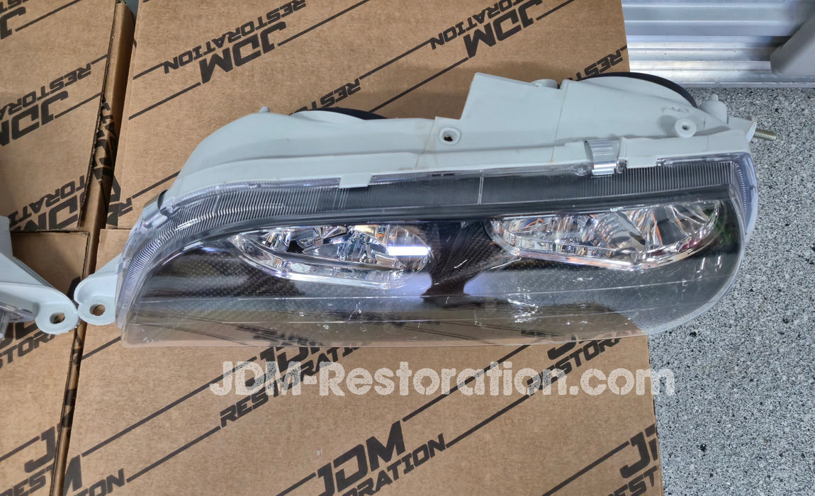 Car headlights on a cardboard box with JDM Restoration.com branding against a metallic background.