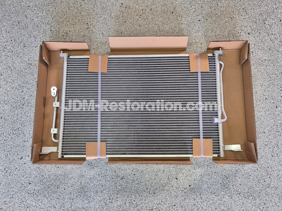 Car air conditioning condenser in a cardboard box on a concrete floor with 'JDM Restoration.com' branding.
