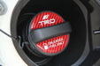 A close-up of a black and red carbon-fiber-patterned fuel cap with white TRD and 'UNLEADED FUEL ONLY' text, set inside a dark circular opening.