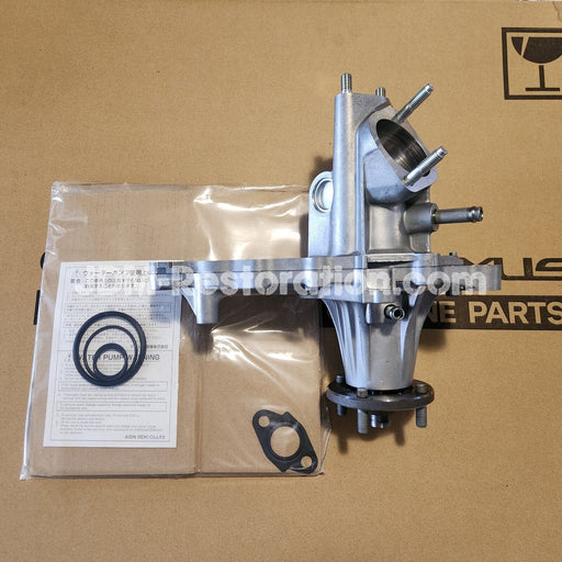 A new Toyota Jzx100 1JZGTE water pump complete assembly with gaskets and seals, displayed on a cardboard surface, indicating it is either being installed or has been removed from the vehicle.