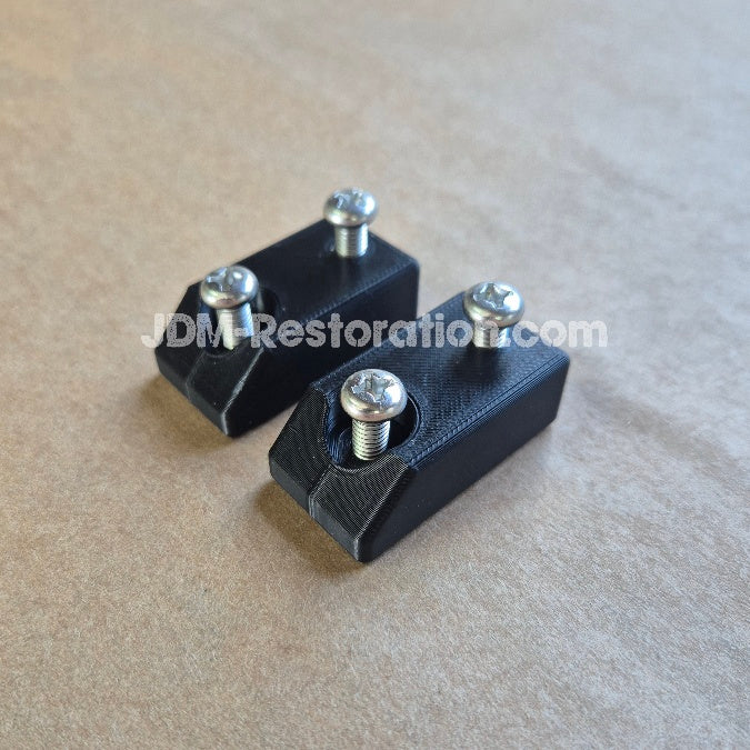 Two black rectangular metal mounting brackets with silver screws, shown on a textured tan background. A watermark 'JDMRestoration.