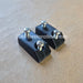 Two small black plastic electronic components with silver screws, displayed on a textured brown surface with a JDM- Restoration watermark.