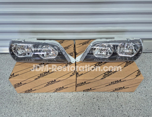 Car headlights on a cardboard box with JDM Restoration.com branding against a metallic background.