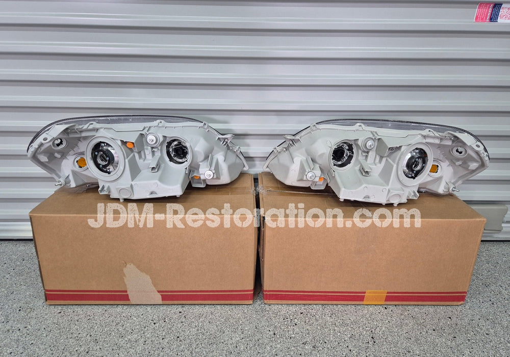 Two car headlight assemblies on cardboard boxes with 'JDM Restoration.com' branding.
