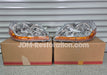 Two car headlights on cardboard boxes with 'JDM-Restoration.com' branding.