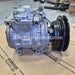 A silver and black automotive air conditioning compressor pulley assembly resting on a cardboard box printed with Lexus and Toyota branding. A translucent JDM Restoration watermark is visible across the center.