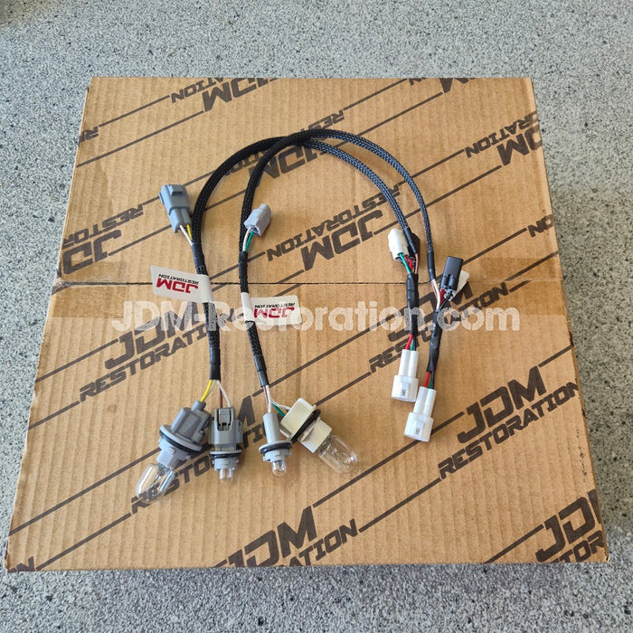 A set of automotive wiring harnesses with multiple connectors and bulbs, laid out on top of a brown cardboard box printed with 'JDM RESTORATION'.