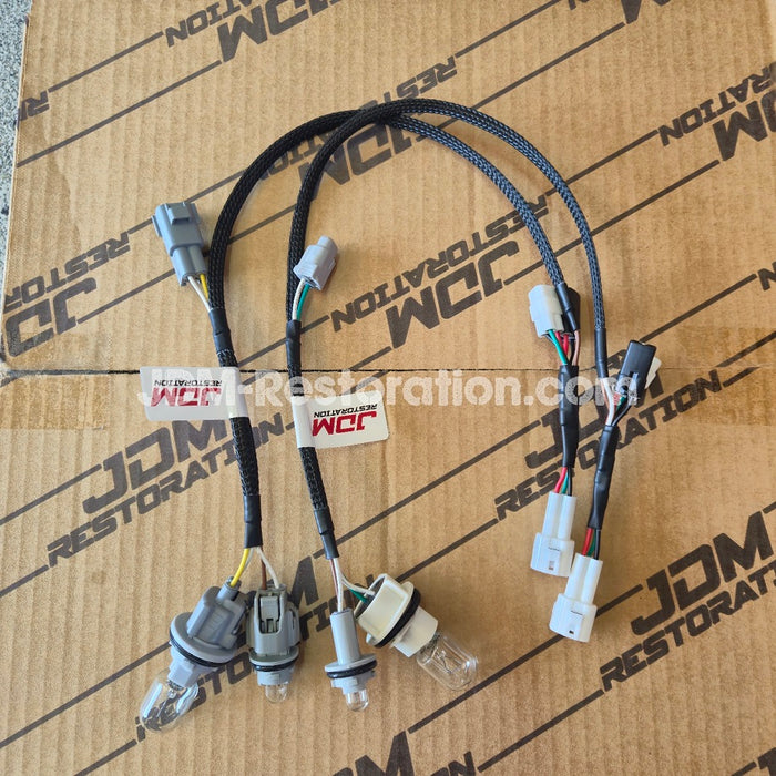 A pair of automotive wiring harnesses with multiple connectors and bulbs, laid out on a brown cardboard box printed with 'JDM Restoration'.