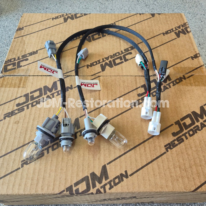 A wiring harness kit with multiple black braided wires, plastic connectors, and small bulbs, laid out on top of a brown cardboard box printed with JDM Restoration branding.