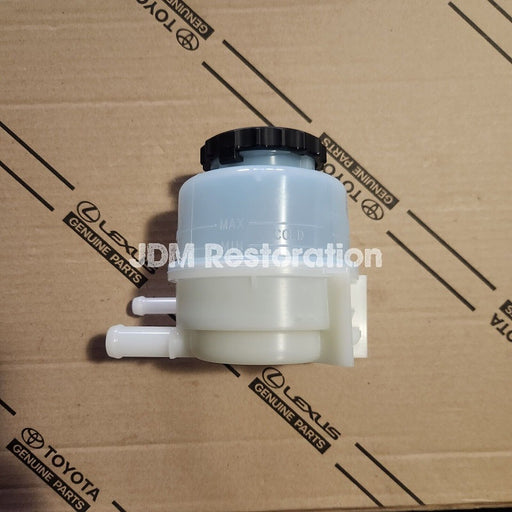 A new white power steering reservoir for Toyota vehicles, placed on a cardboard box with the text 'JDM Restoration' visible.